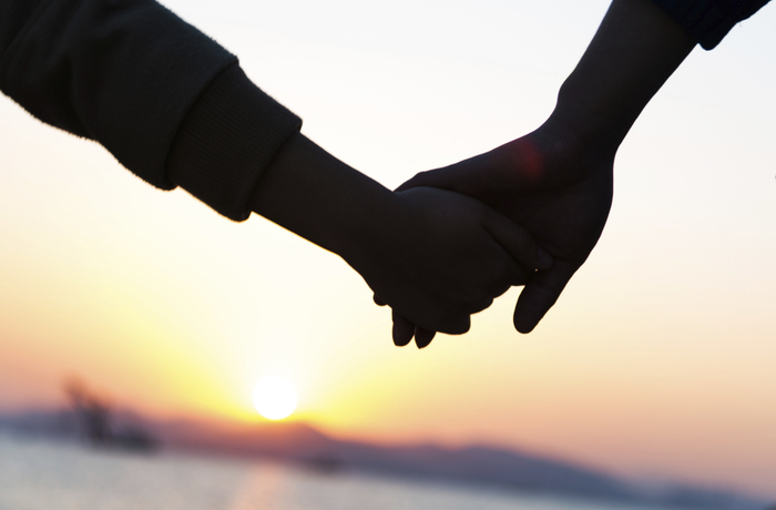 A couple holding hands in front of the sea at sunset.